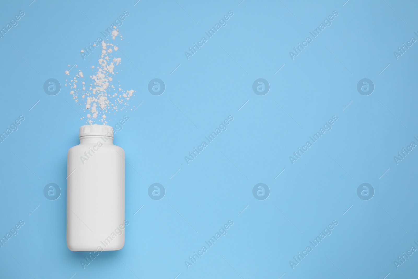 Photo of Bottle and scattered dusting powder on light blue background, top view with space for text. Baby cosmetic product