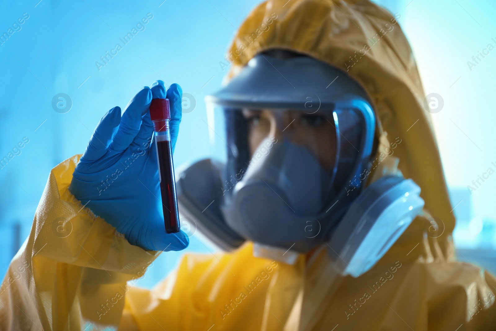 Photo of Scientist in chemical protective suit holding test tube with blood sample at laboratory, focus on hand. Virus research