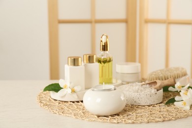 Composition with beautiful jasmine flowers and skin care products on white wooden table indoors