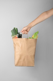 Photo of Woman holding paper bag with fresh vegetables on grey background, closeup