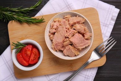 Bowl with canned tuna, tomatoes and rosemary on black wooden table, flat lay