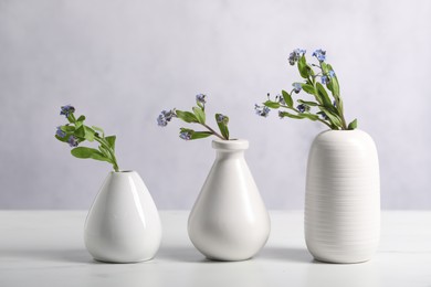 Photo of Beautiful forget-me-not flowers in vases on white marble table, closeup