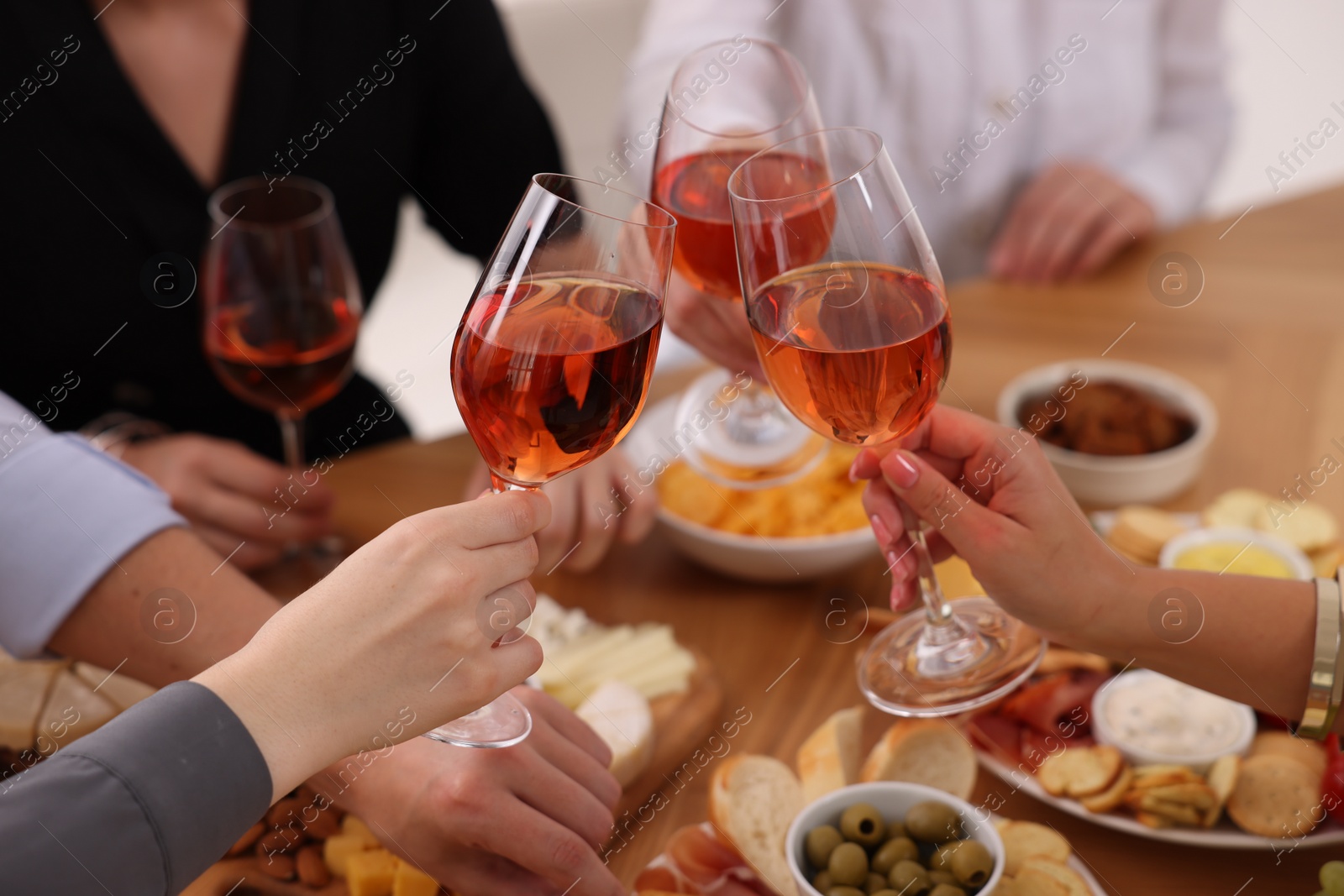 Photo of People clinking glasses with rose wine above table indoors, closeup
