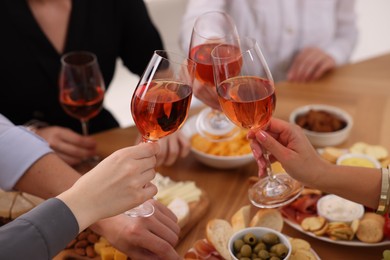 People clinking glasses with rose wine above table indoors, closeup