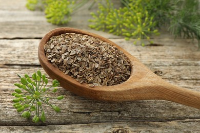 Photo of Spoon with dry seeds and fresh dill on wooden table, closeup