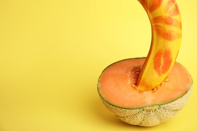 Photo of Fresh banana with red lipstick marks and melon on yellow background, space for text. Sex concept