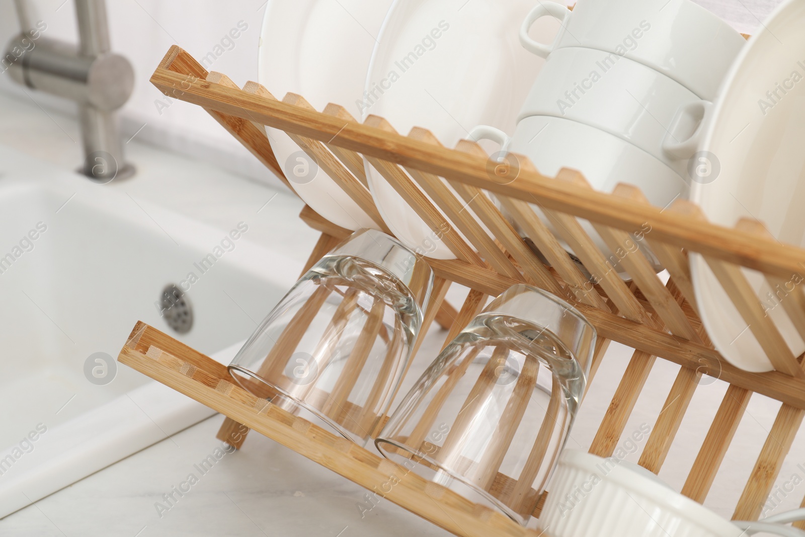 Photo of Drying rack with clean dishes on countertop near sink in kitchen, closeup