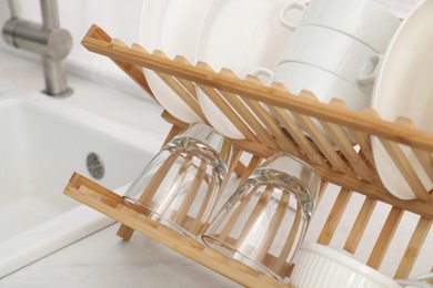Drying rack with clean dishes on countertop near sink in kitchen, closeup