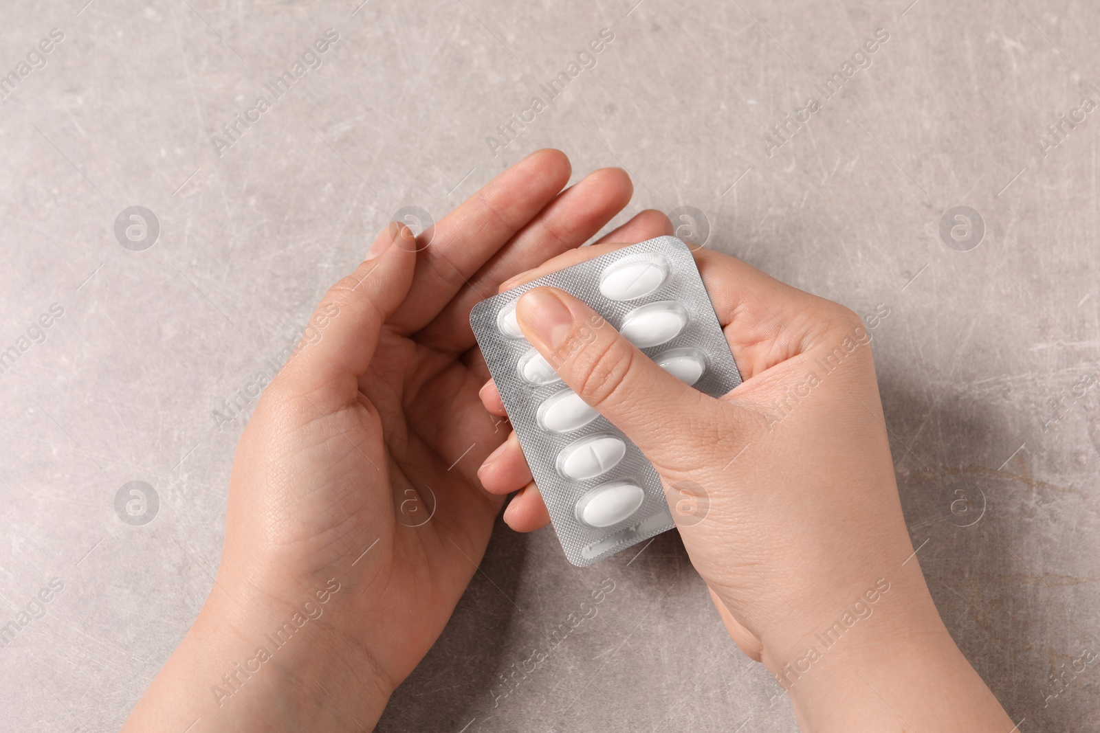 Photo of Woman with blister of white pills at grey table, closeup