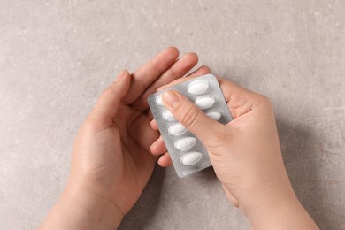 Woman with blister of white pills at grey table, closeup