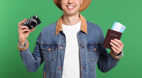 Smiling man with passport, tickets and camera on green background, closeup