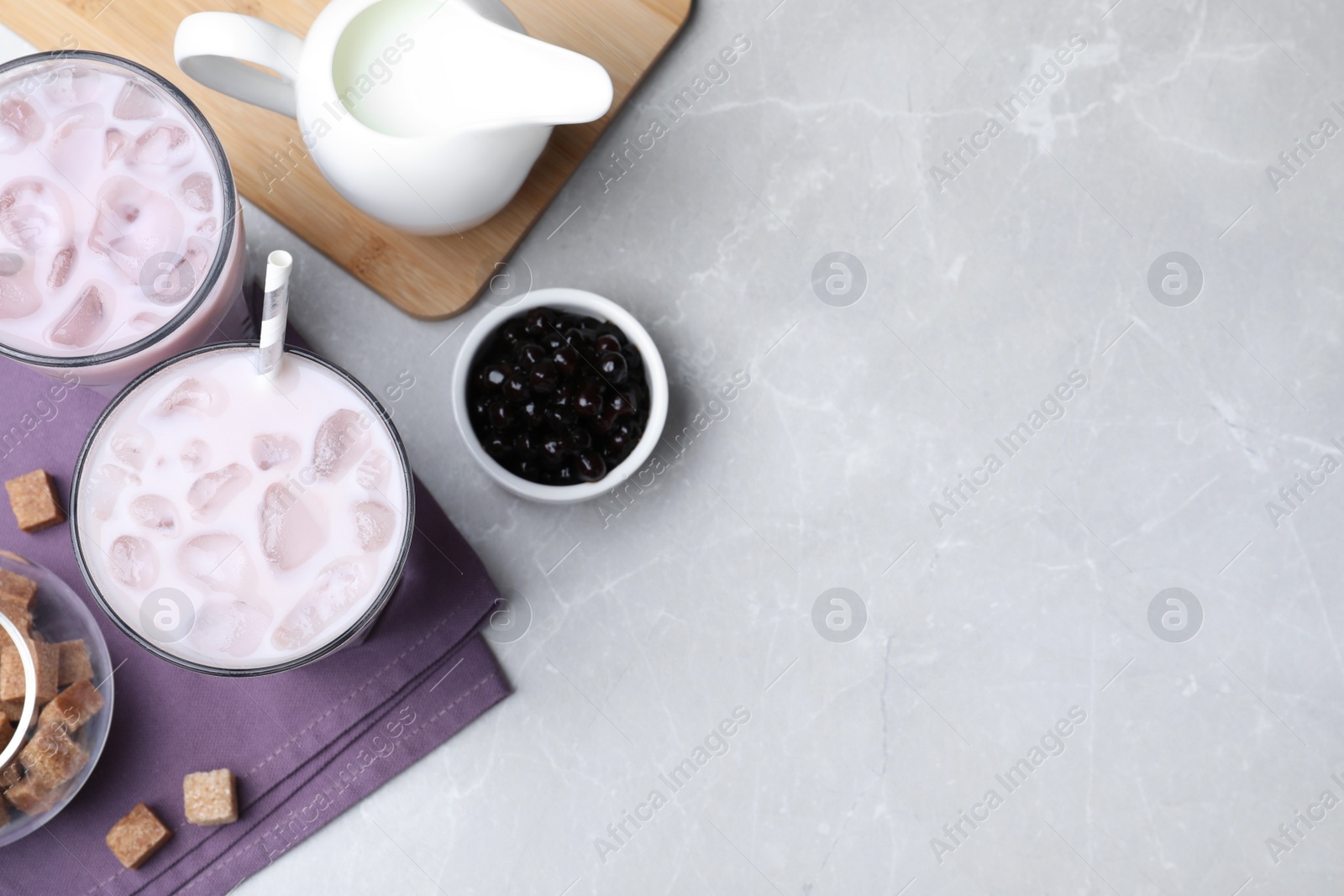 Photo of Bubble milk tea and bowl with tapioca balls on light grey marble table, flat lay. Space for text