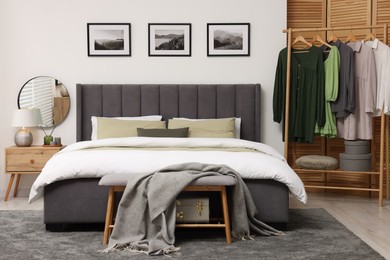 Photo of Comfortable bed and clothes on rack in stylish room