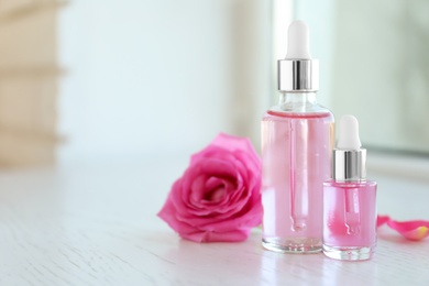 Photo of Bottles of rose essential oil and fresh flower on window sill, space for text