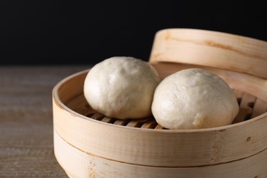 Photo of Delicious Chinese steamed buns in bamboo steamer on wooden table against black background, closeup