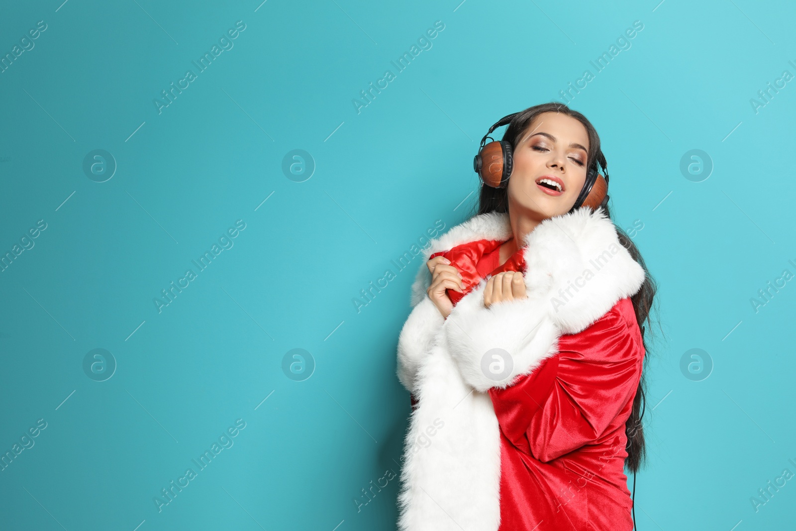 Photo of Young woman in Santa costume listening to Christmas music on color background