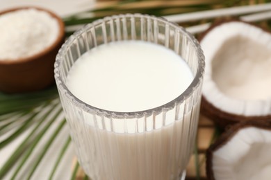 Photo of Glass of delicious vegan milk, coconuts and leaf on table, closeup