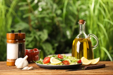 Bottle with cooking oil and delicious salad on wooden table against blurred background