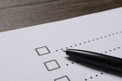 Photo of Paper sheet with checkboxes and pen on wooden table, closeup. Checklist