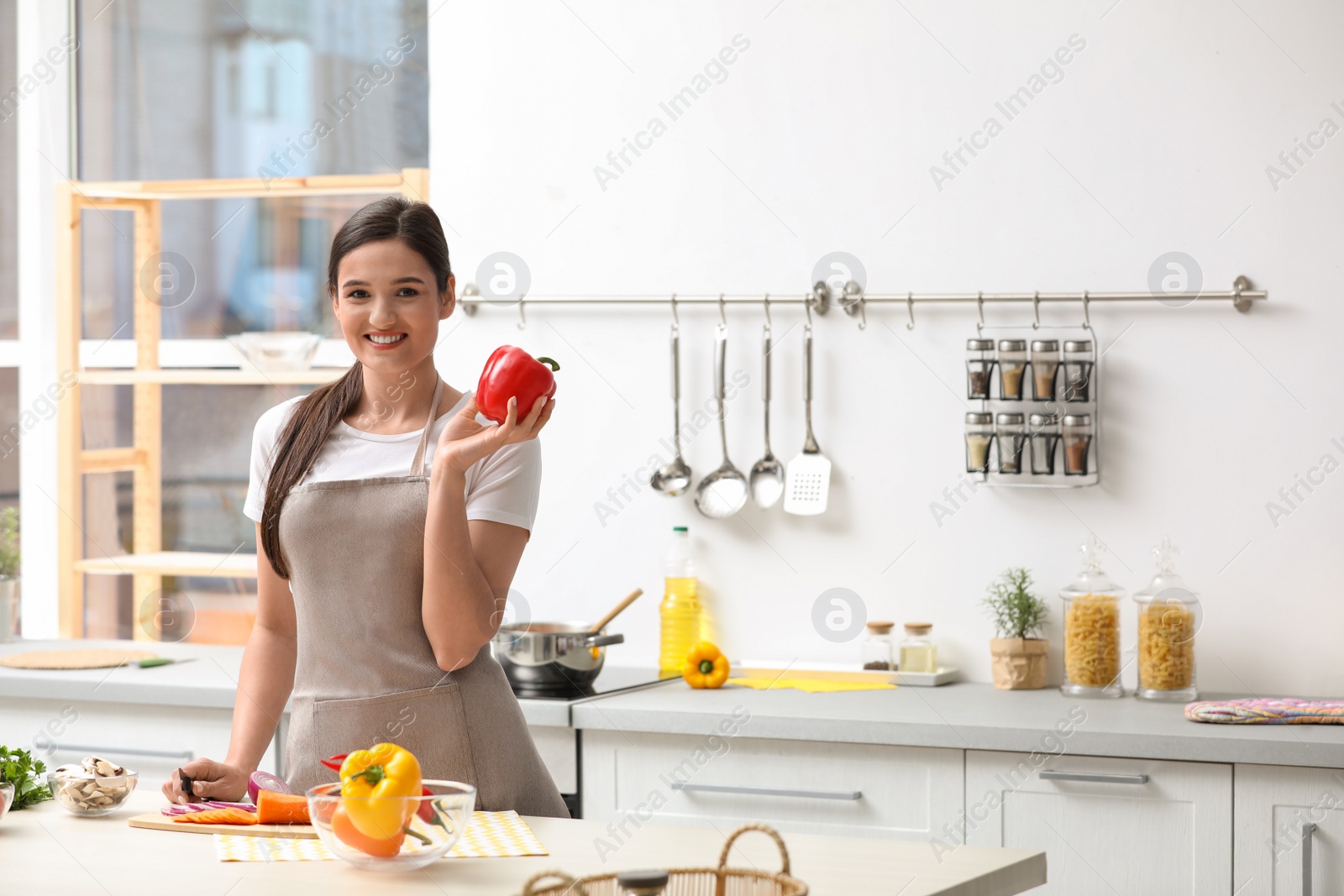 Photo of Young woman with bell pepper at table in kitchen, space for text. Cooking soup