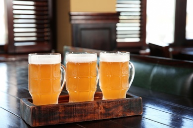 Glasses of tasty beer on wooden table in bar