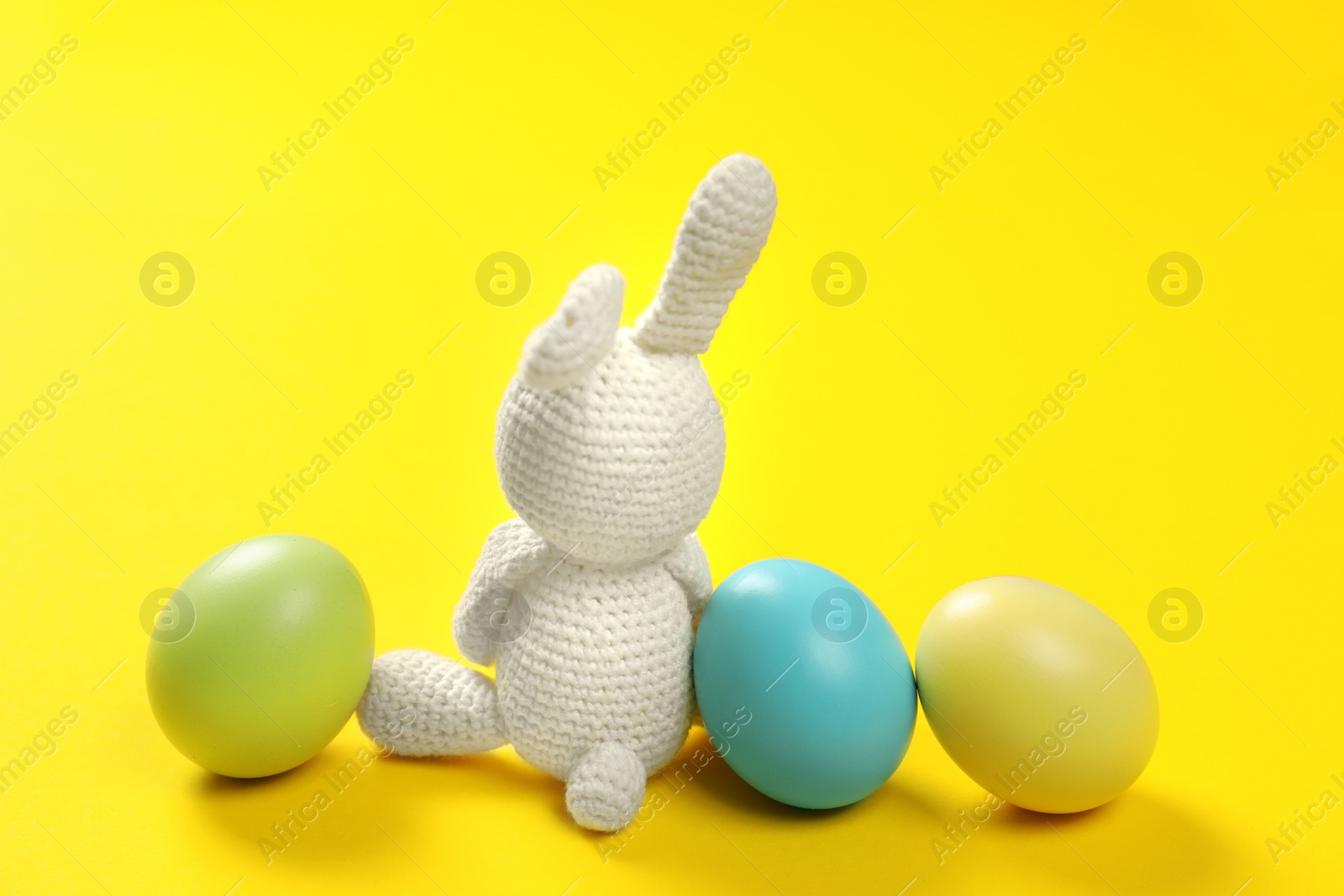 Photo of Cute Easter bunny toy and dyed eggs on color background