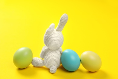 Cute Easter bunny toy and dyed eggs on color background