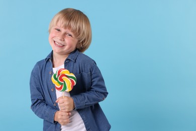Happy little boy with colorful lollipop swirl on light blue background, space for text
