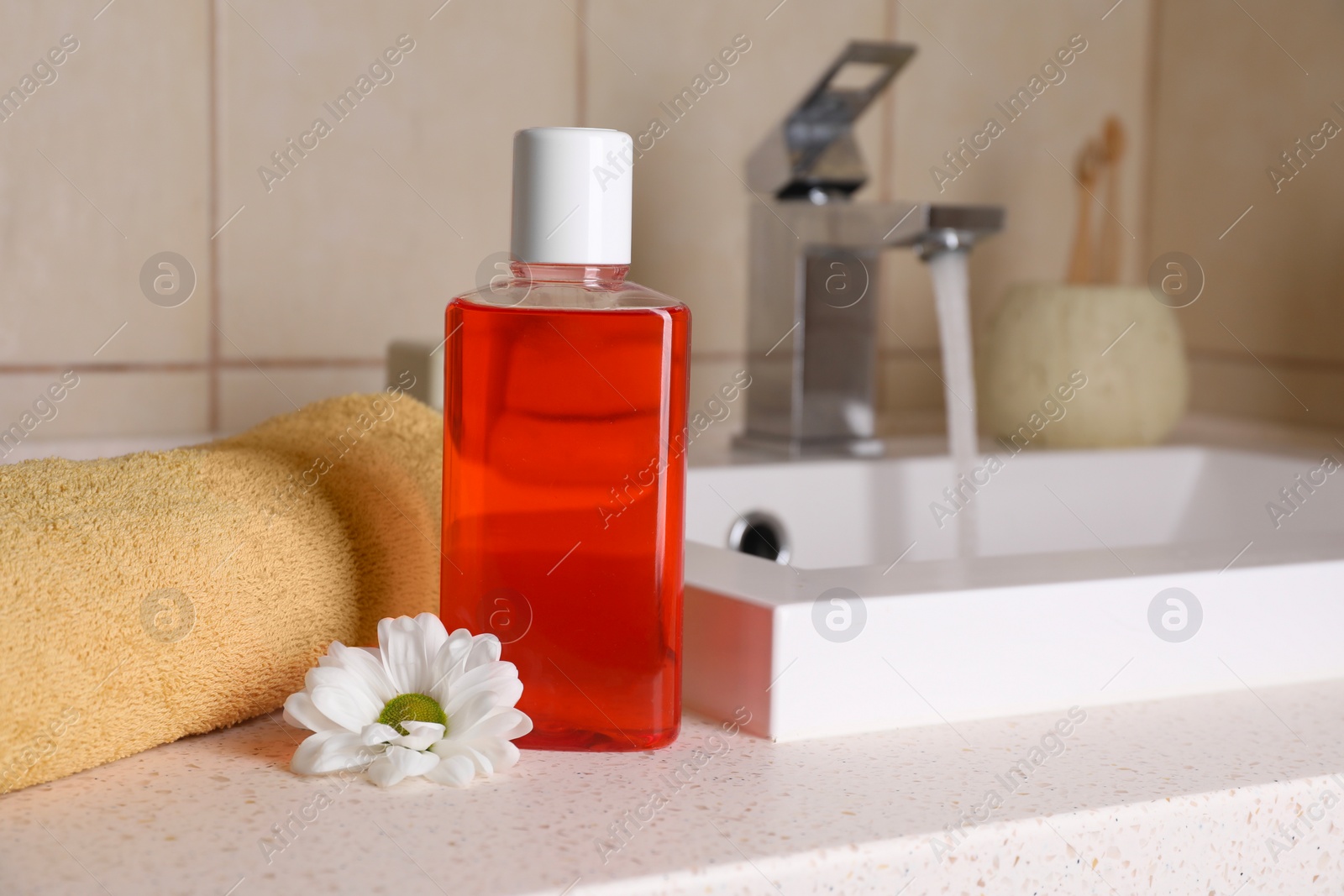 Photo of Fresh mouthwash in bottle, chamomile and towel on countertop near sink in bathroom, closeup