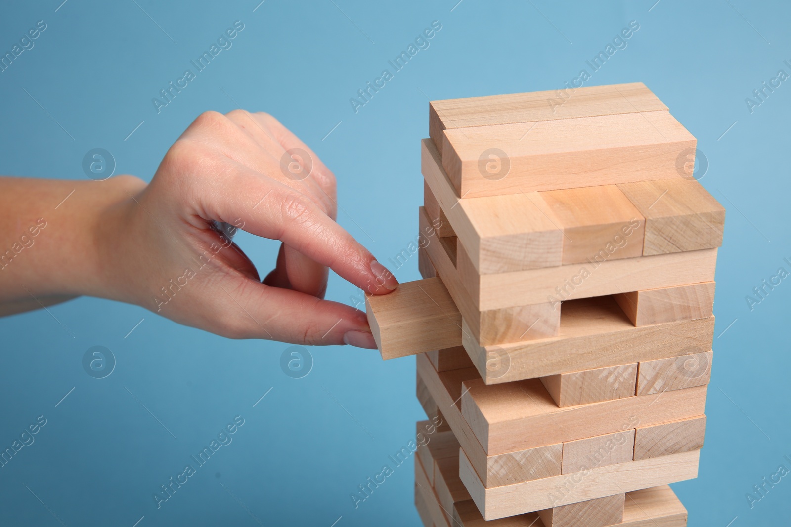 Photo of Woman playing Jenga on light blue background, closeup