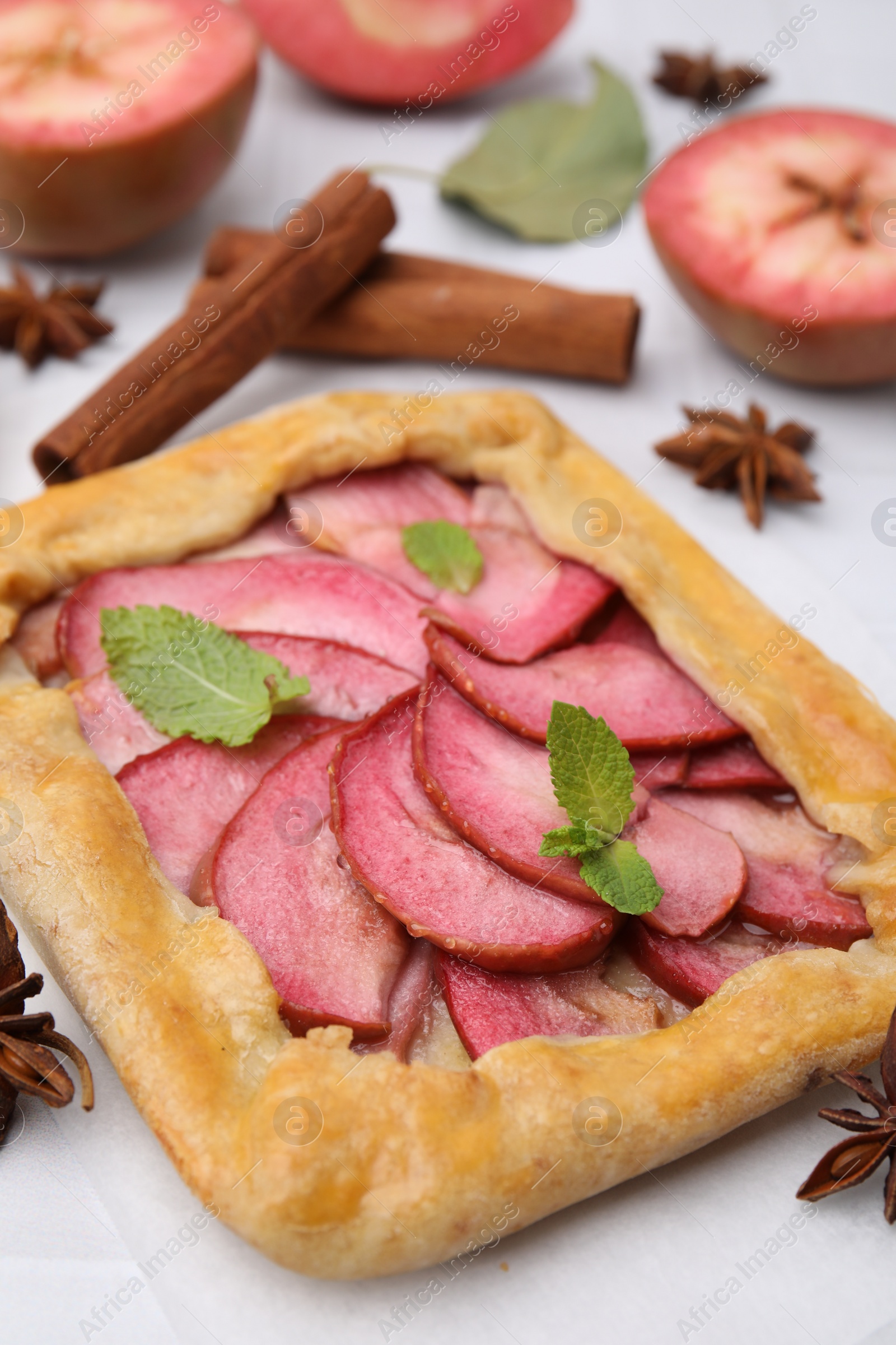Photo of Delicious apple galette with mint and ingredients on white tiled table, closeup