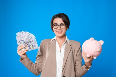 Photo of Young woman in eyeglasses with money and piggy bank on light blue background