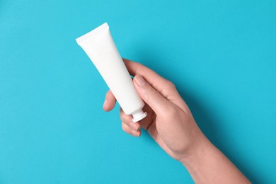 Photo of Woman with tube of hand cream on light blue background, top view