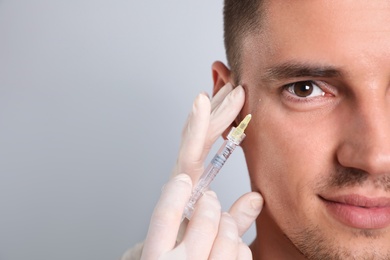 Photo of Man getting facial injection on grey background, closeup. Cosmetic surgery