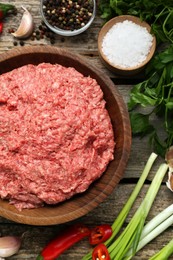 Photo of Bowl with raw fresh minced meat and ingredients on wooden table, flat lay