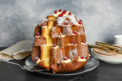 Photo of Taking slice of delicious Pandoro Christmas tree cake with powdered sugar and berries on black table