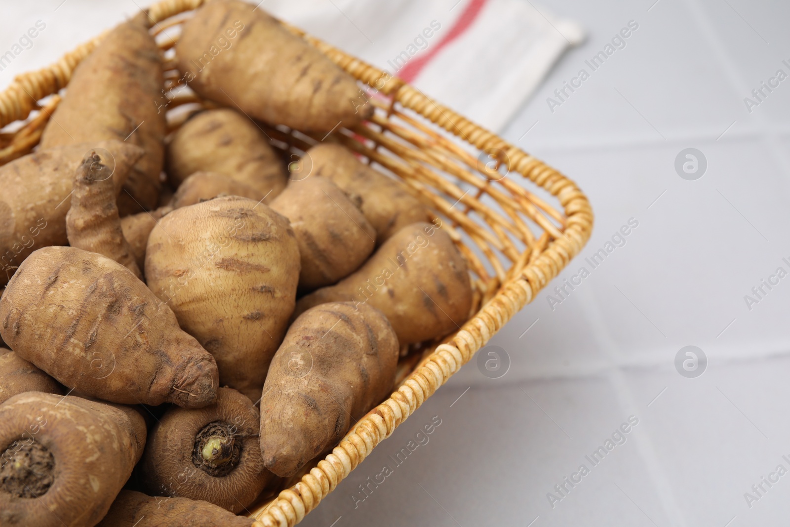 Photo of Tubers of turnip rooted chervil in wicker basket on white tiled table, closeup