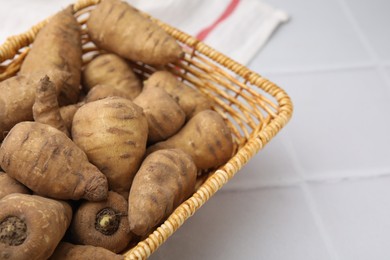 Tubers of turnip rooted chervil in wicker basket on white tiled table, closeup