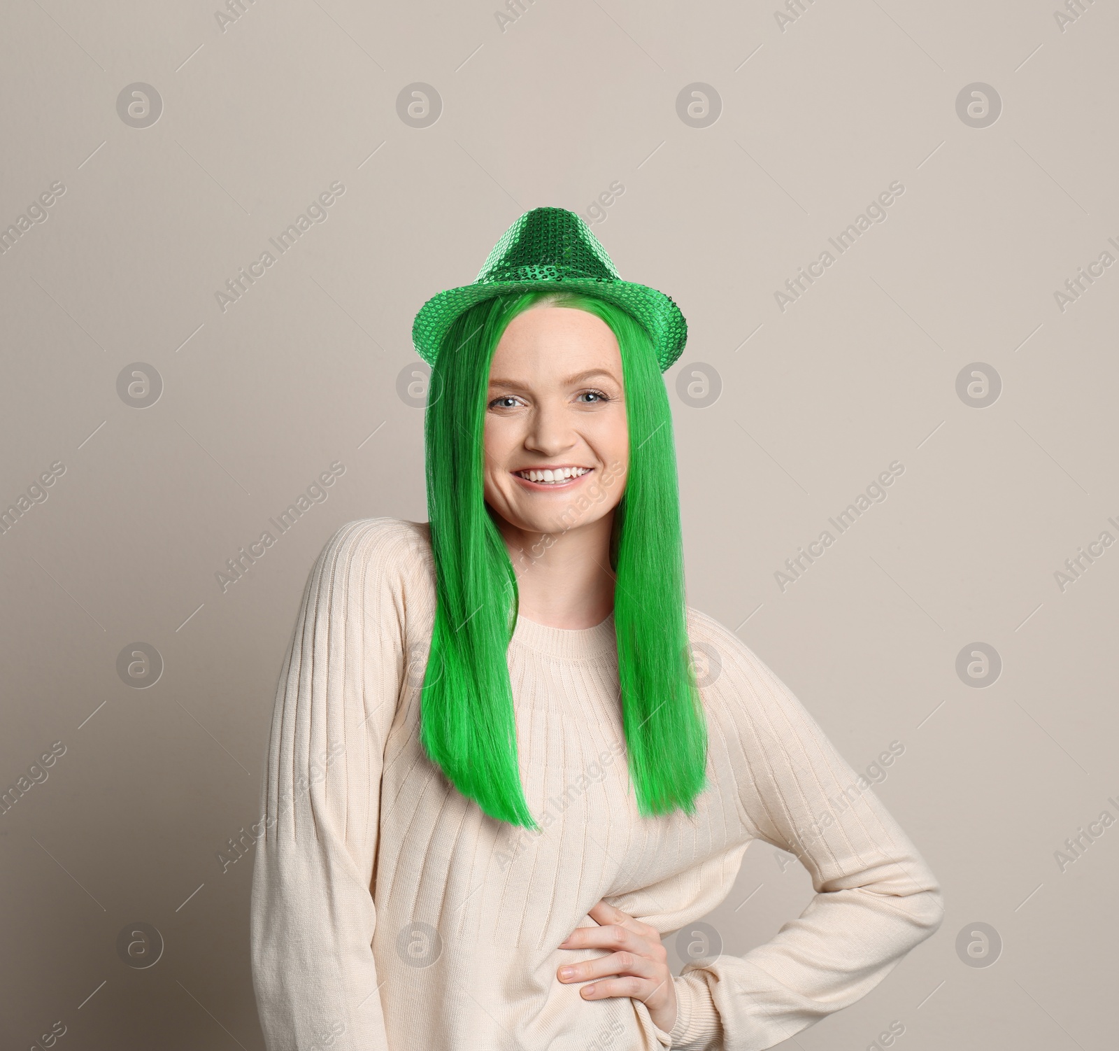 Image of St. Patrick's day party. Pretty woman with green hair and leprechaun hat on grey background