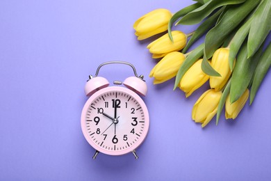Pink alarm clock and beautiful tulips on violet background, flat lay. Spring time