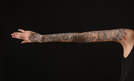 Woman with colorful tattoos on arm against black background, closeup