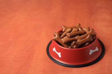 Photo of Red bowl with bone shaped dog cookies on wooden table, space for text