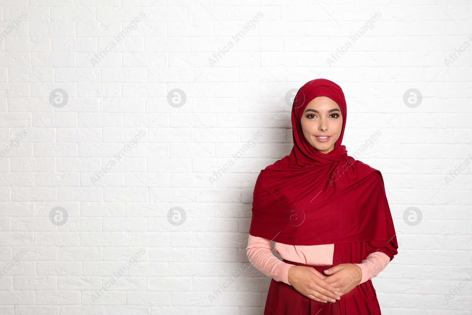 Photo of Portrait of young Muslim woman in hijab against brick wall. Space for text