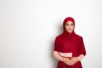 Portrait of young Muslim woman in hijab against brick wall. Space for text