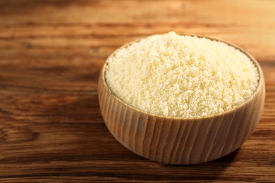 Photo of Bowl with grated parmesan cheese on wooden table, closeup. Space for text