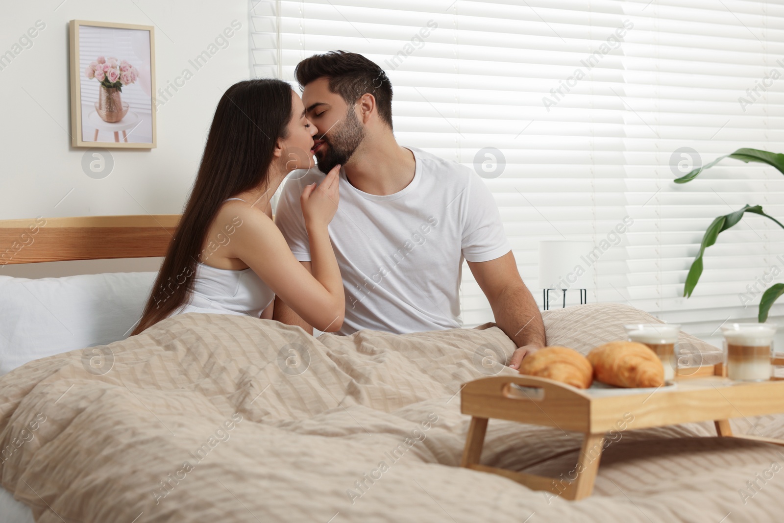 Photo of Happy couple spending time together on bed near wooden tray with breakfast at home