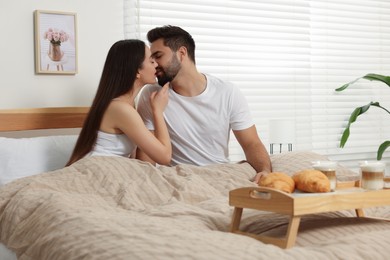 Photo of Happy couple spending time together on bed near wooden tray with breakfast at home