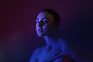 Portrait of beautiful young woman on color background in neon lights