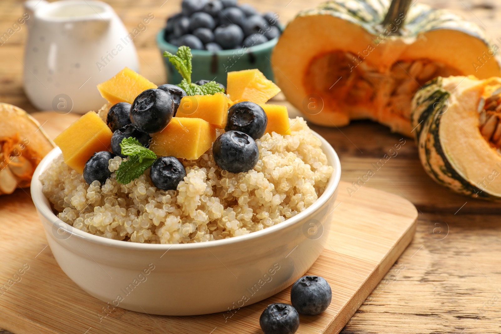 Photo of Tasty quinoa porridge with blueberries, pumpkin and mint in bowl on wooden table, closeup