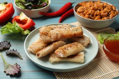 Photo of Tasty fried spring rolls and ingredients on light blue wooden table, closeup